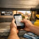 Manos sosteniendo un smartphone negro buscando opciones de mantenimiento para puertas de garaje en Barcelona, con fondo desenfocado.